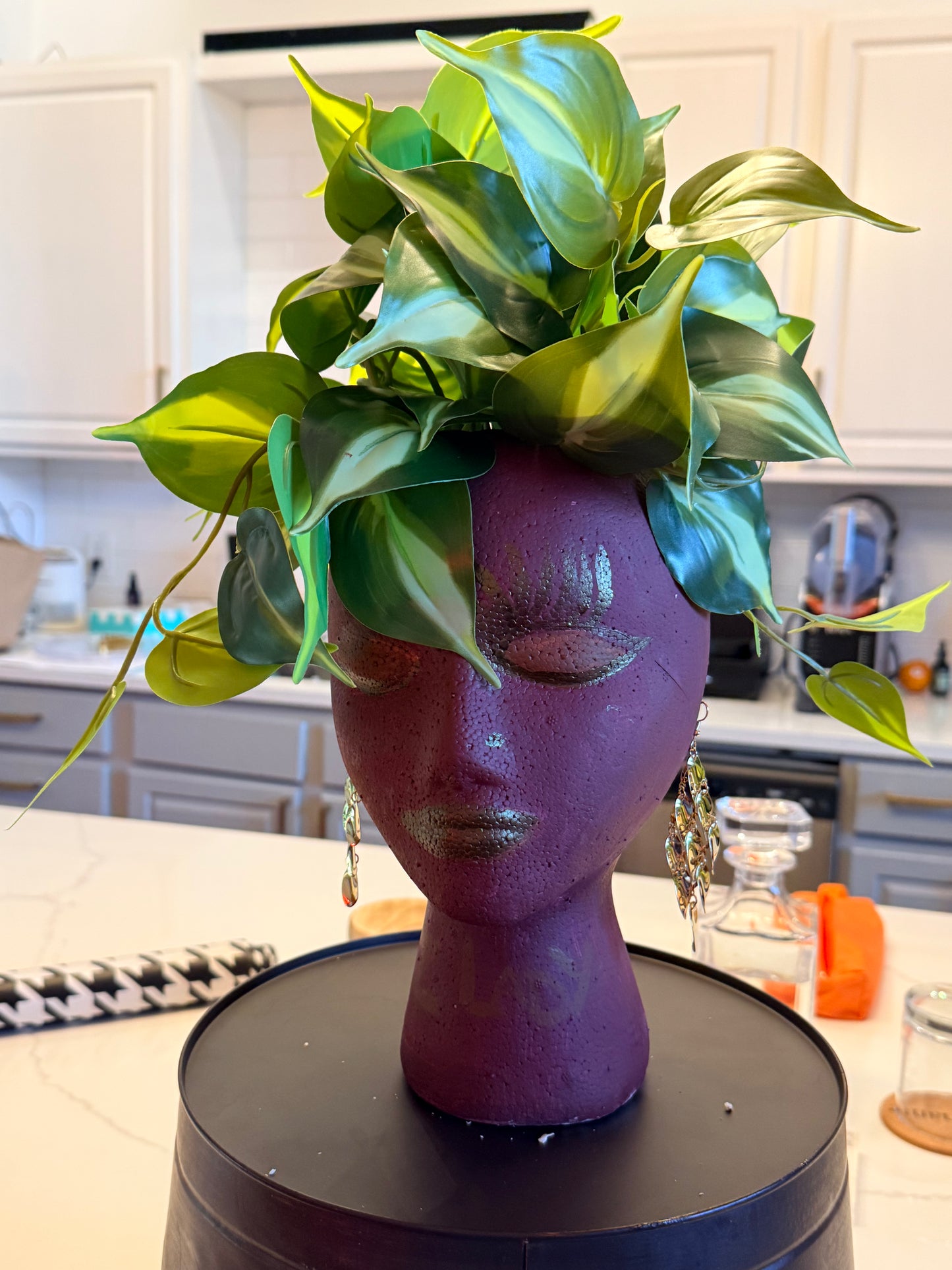 Purple head-shaped vase with green leaves on a kitchen counter