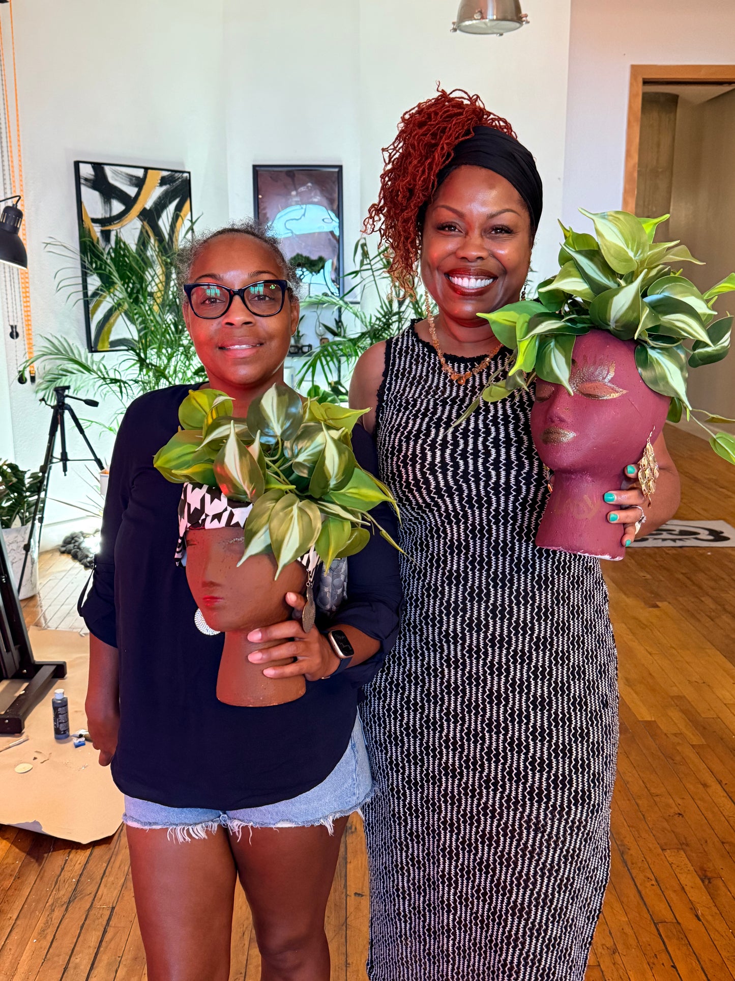 Two women holding planters with green plants indoors.