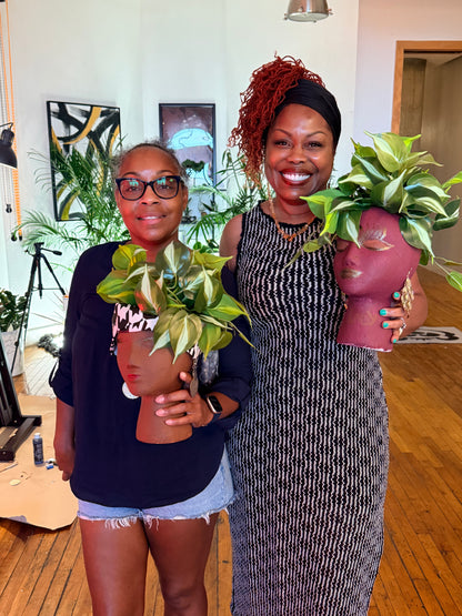 Two women holding planters with green plants indoors.